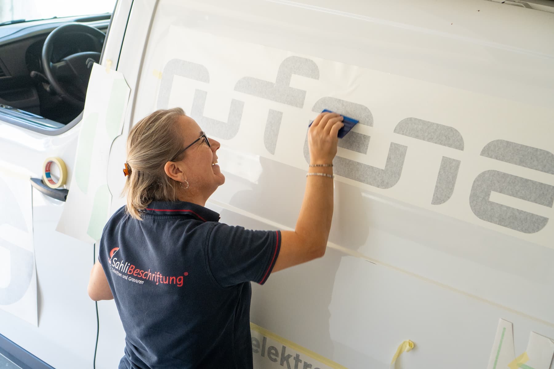 Mitarbeiterin von SahliBeschriftung appliziert den Schriftzug «rüfenacht» auf die Seitenwand eines Lieferwagens